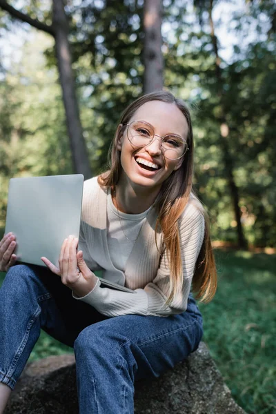 快乐的女人 戴着眼镜 一边笑一边拿着笔记本电脑 在公园里看着相机 — 图库照片