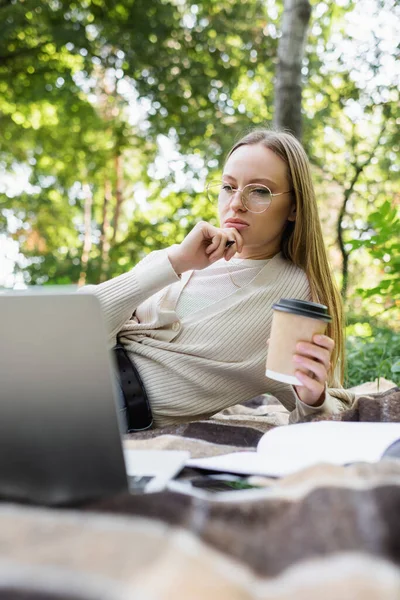Pensive Woman Glasses Holding Paper Cup Looking Laptop Blanket Park — Stok fotoğraf