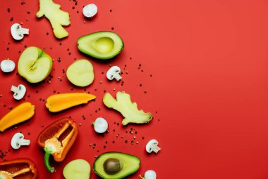 Flat lay of cut fruits and vegetables near peppercorns on red background