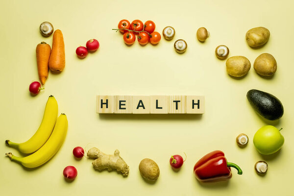 Top view of cubes with health lettering near organic food on yellow background 