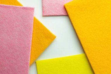 close up view of orange, pink and yellow dishcloths on white background, top view