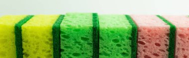 close up view of porous yellow, green and pink sponges isolated on grey, banner