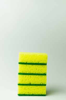 stack of porous yellow and green sponge scourers on grey background