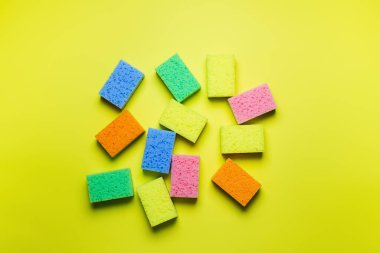 plenty of bright multicolored sponges on yellow background, top view