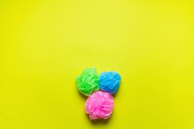 top view of pink, blue and green body puffs on yellow background with copy space