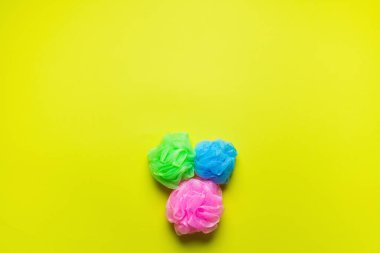 top view of pink, blue and green body puffs on yellow background with copy space clipart