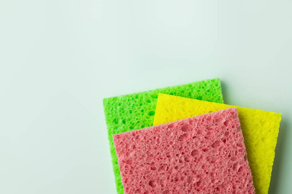 top view of pink, yellow and green sponge cloths on grey background