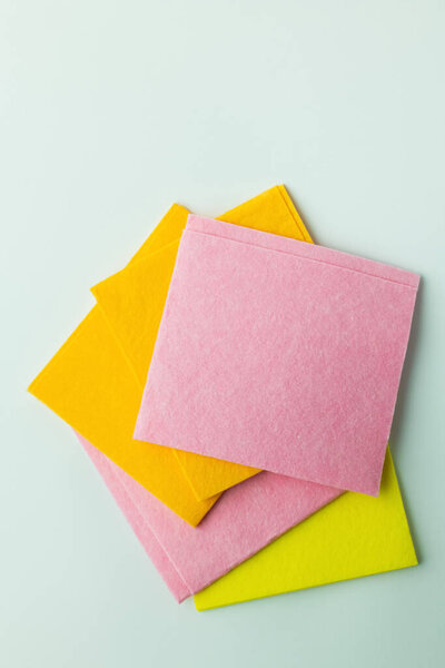 top view of pink, orange and yellow dishcloths on grey background