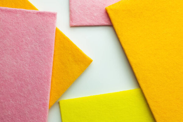close up view of orange, pink and yellow dishcloths on white background, top view