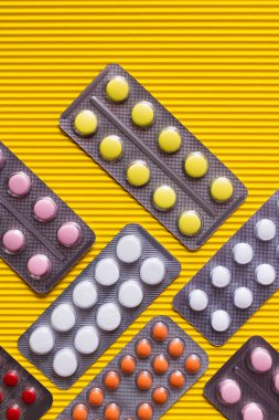 Sarı desenli arka planda farklı renkli haplarla dolu su toplayıcı paketlerinin üst görüntüsü 