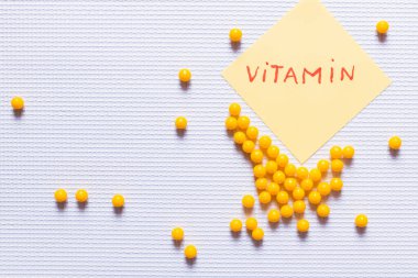 top view of yellow round shape medication near paper note with vitamin lettering on white textured background