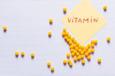 top view of yellow round shape medication near paper note with vitamin lettering on white textured background clipart
