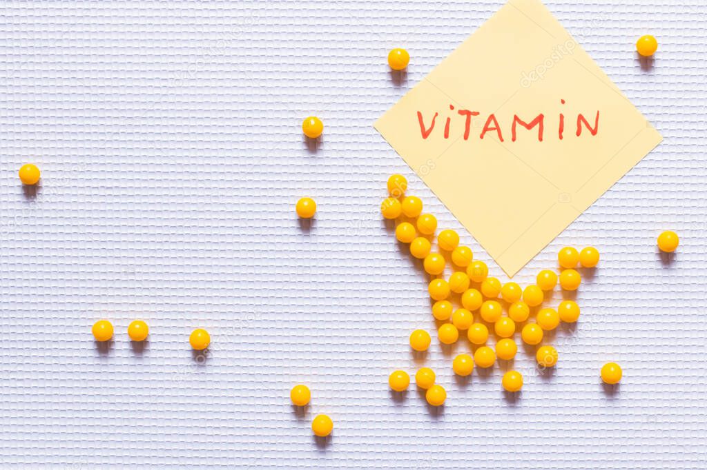 top view of yellow round shape medication near paper note with vitamin lettering on white textured background