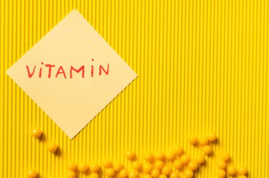 top view of round shape medication near paper note with vitamin lettering on yellow textured background