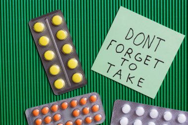 top view of blister packs with pills near paper note with dont forget to take lettering on textured green background clipart