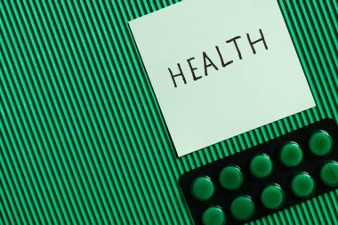 top view of blister pack with pills near paper note with health lettering on textured green background
