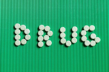 top view of drug word made of yellow round shape medication on green textured background