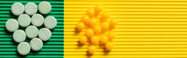 top view of round shape pills and vitamins on textured green and yellow background, banner clipart