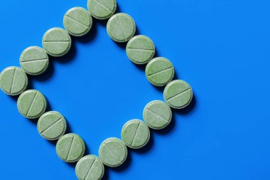 top view of green pills in shape of rhombus on bright blue background