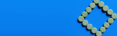 top view of green pills in shape of rhombus on bright blue background, banner