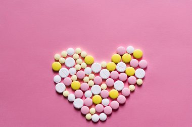 Pembe arka planda kalp şeklinde farklı yuvarlak hapların düz görünümü 