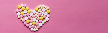 Pembe arka planda kalp şeklinde farklı yuvarlak hapların düz görünümü, afiş