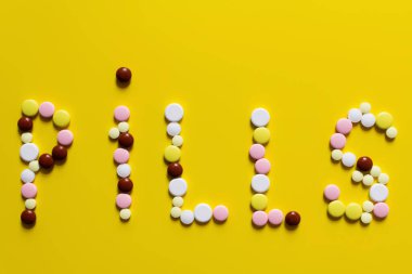 top view of pills word made of colorful round shape medication on yellow background