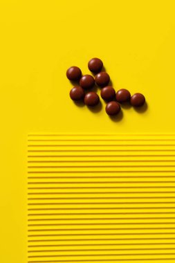 top view of pile with dark round shape pills on yellow and textured background 