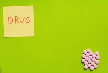 top view of pink round shape medication near paper note with drug lettering on green background