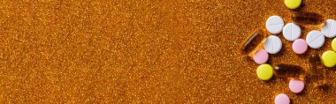 top view of different colorful pills on shiny golden background, banner