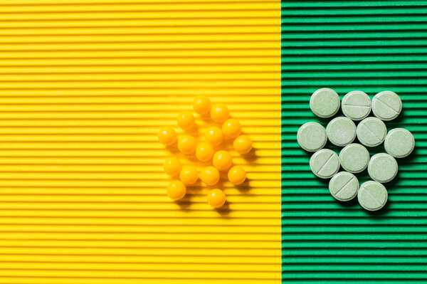 top view of round shape pills and vitamins on textured yellow and green background