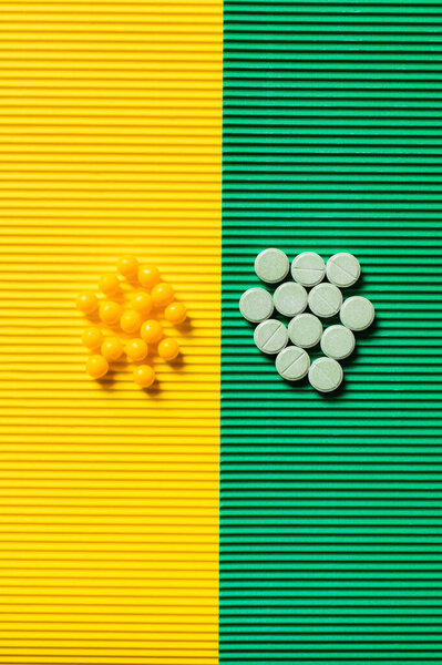 top view of round shape pills and vitamins on textured green and yellow background