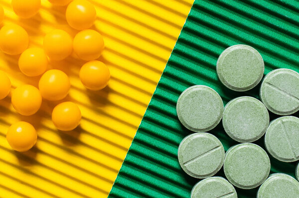 close up view of round shape pills and vitamins on textured green and yellow background