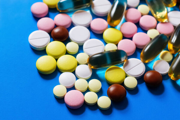 close up view of different colorful pills and capsules on bright blue background