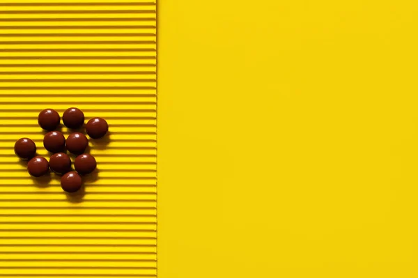 黄色のテクスチャの背景に茶色の丸い形の丸薬の山のトップビュー — ストック写真