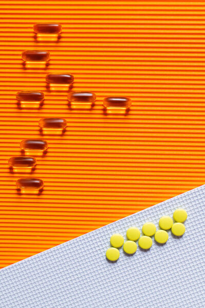 flat lay of yellow pills on and jelly capsules on white and orange textured background