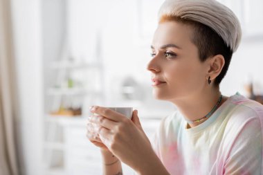 Genç ve şık bir kadın elinde bir fincan kahve tutuyor.