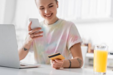 blurred woman with credit card and smartphone near laptop and glass of orange juice