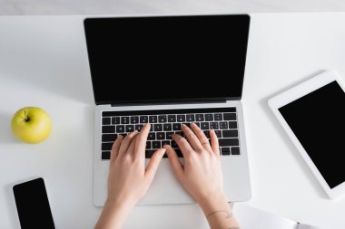 Akıllı telefonun, dijital tabletin ve taze elmanın yanında dizüstü bilgisayarda yazan kadının üst görünümü