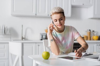 Gülümseyen kadın elmanın yanında cep telefonuyla konuşurken dijital tableti işaret ediyor