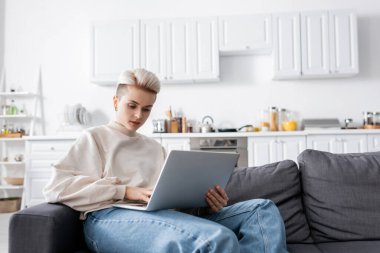 young woman using laptop on couch in open plan kitchen clipart