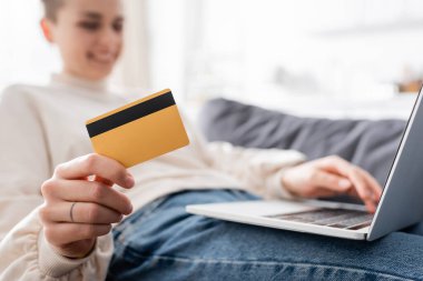 Seçici kredi kartı ve laptop odağı bulanık arka planda gülümseyen bir kadının yanında