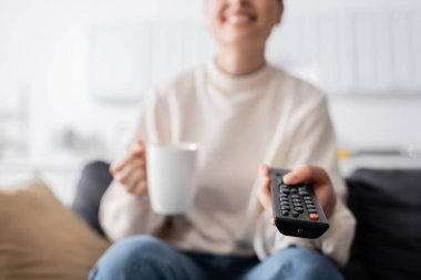 Bir fincan çayla gülümseyen kadın görüntüsü. Televizyon kanalları tıklaması, bulanık arka plan.