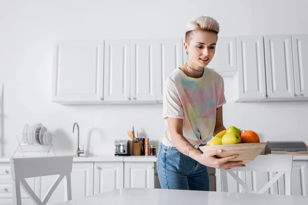 正の女性でTシャツを保持ボウルに新鮮な果物でキッチン — ストック写真