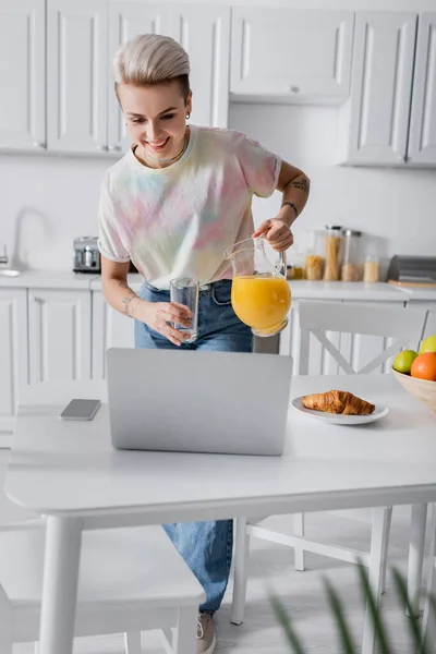 Smiling Woman Glass Jug Orange Juice Looking Laptop Smartphone Croissant — Stock Fotó