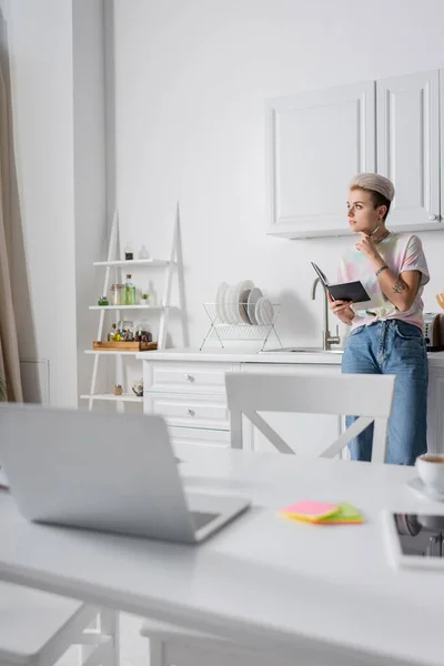 Pensive Woman Notebook Looking Away Kitchen Blurred Laptop Table — Stockfoto