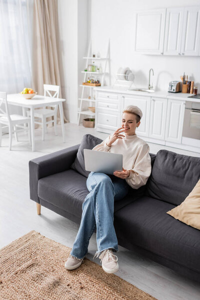 high angle view of woman in jeans sitting with laptop on sofa in open plan kitchen