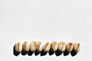 flat lay view of row with salty cracked pistachios on white background