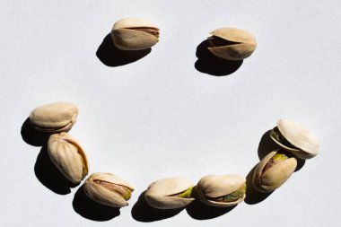 flat lay of cracked green and salty pistachios in shape of smile on white background 