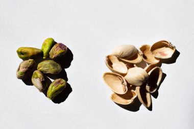 top view of pile with green and salty pistachios near nutshells on white background